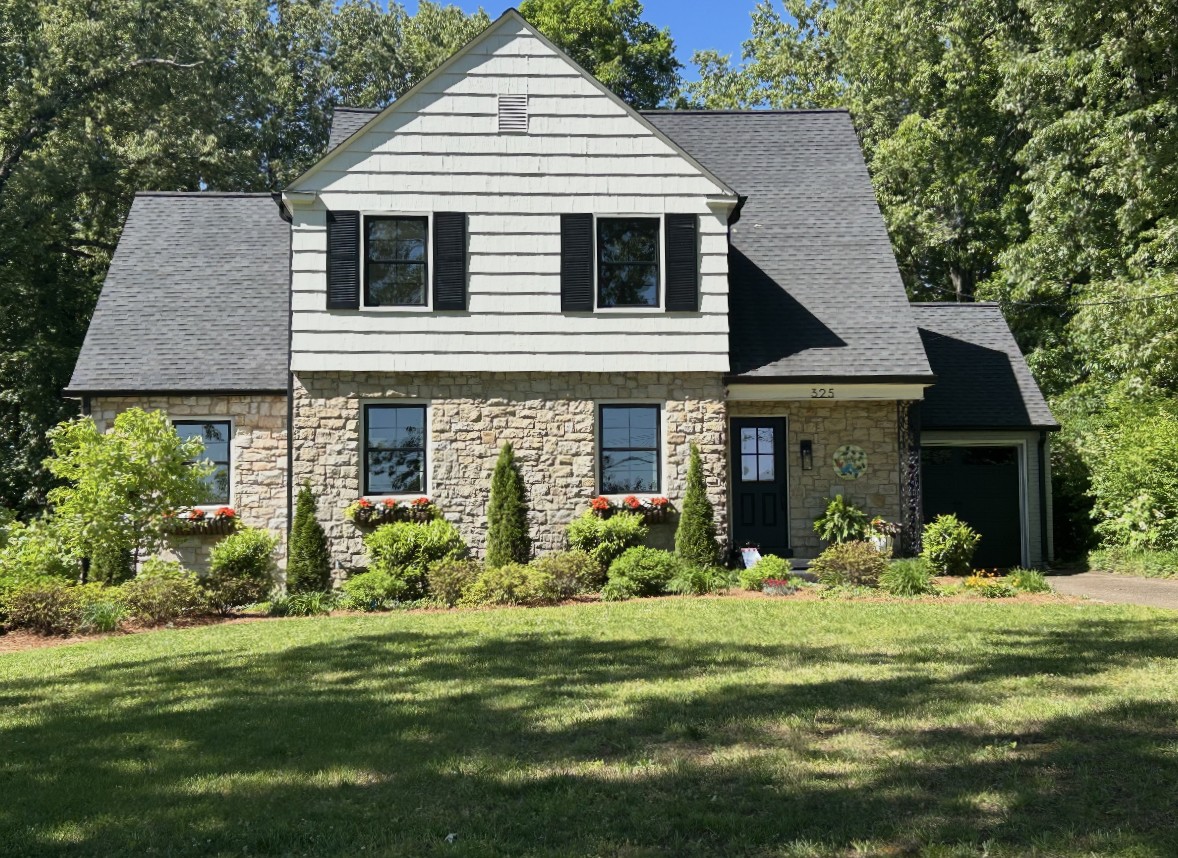Two-story home that with stone on the first story and siding on the second story with a steep roofline. Landscaping involves a m